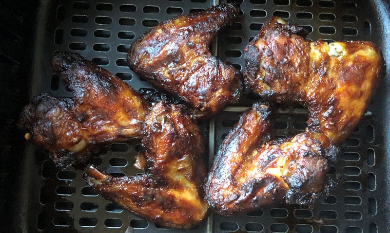 Four whole charred Buffalo chicken wings positioned in air fryer