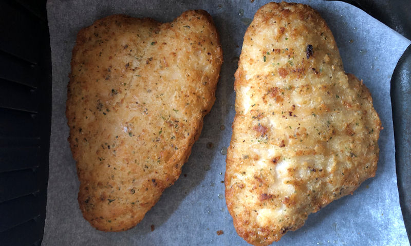 Two battered Basa fish sat on parchment paper inside air fryer basket