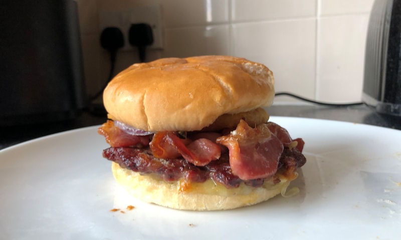 Reheated burger in bun sat on plate near air fryer on countertop